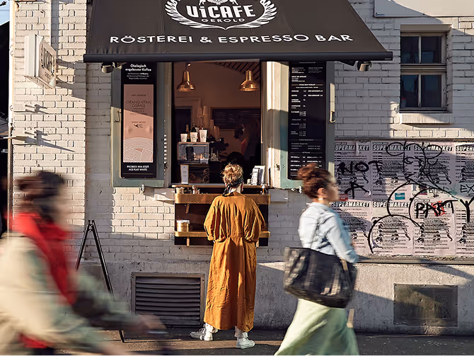 Frau in braunem Mantel bestellt Kaffee am Fenster einer Kaffeerösterei und Espresso-Bar in der Stadt.