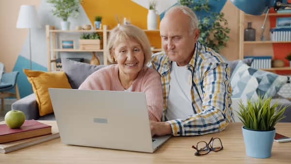 Elderly couple man ans woman are using computer at home talking typing enjoying internet content at home. Technology, people and lifestyle concept.