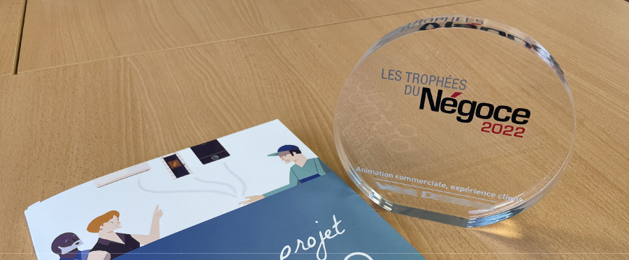 Trophée transparent rond avec inscription Les Trophées du Négoce 2022 posé sur une table en bois à côté d'un document illustré.