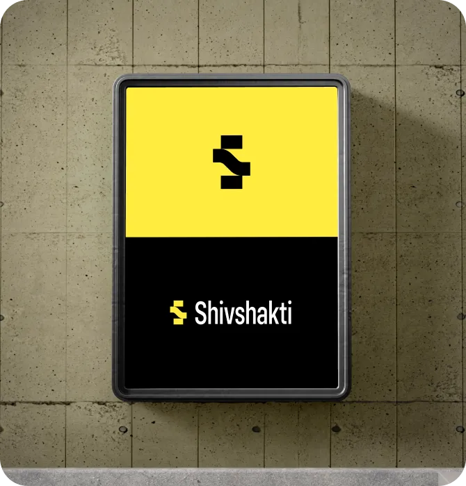 Rectangular sign mounted on a concrete wall with a yellow top half featuring a black abstract symbol and a black bottom half displaying the text 'Shivshakti' with a small yellow and black logo.