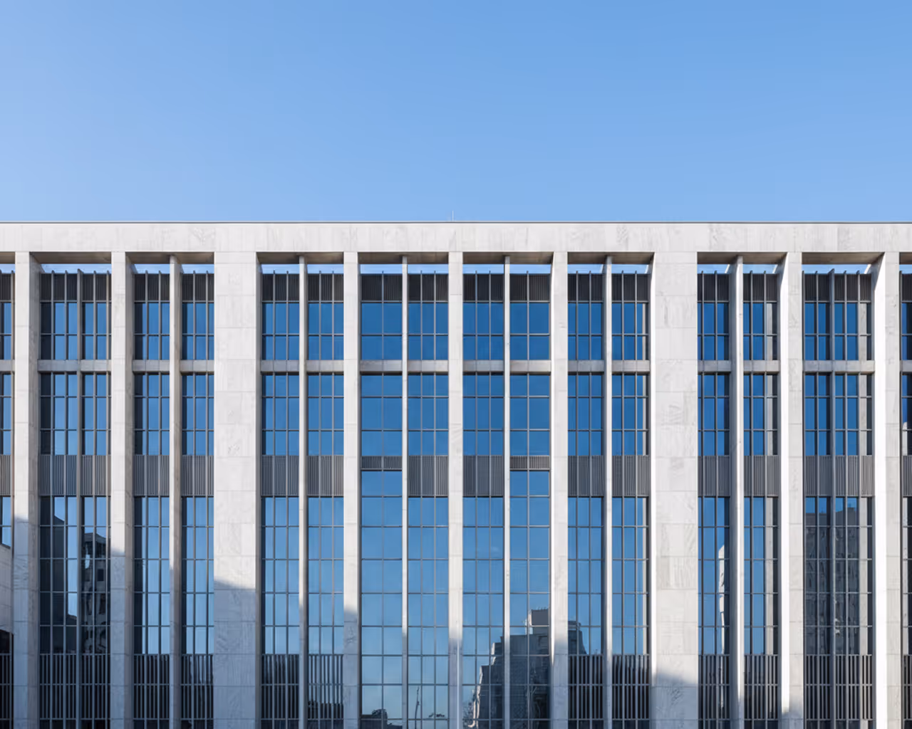 Fachada moderna de edifício com janelas altas e refletoras sob um céu azul claro.