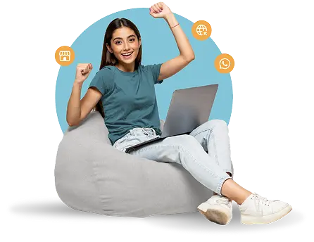 Joven mujer sonriente sentada en una puf gris con una laptop en su regazo, levantando los brazos en celebración.