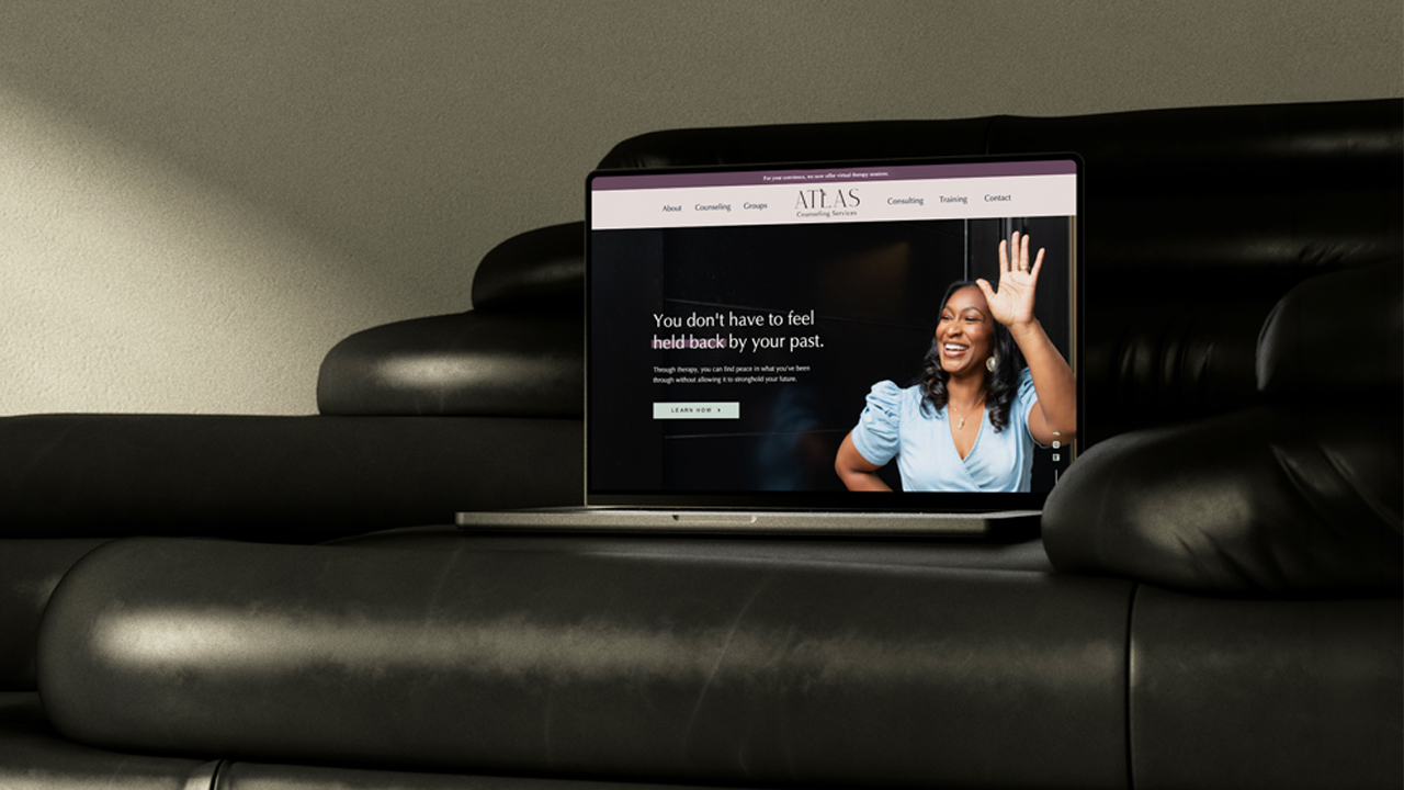 Laptop on a black leather couch displaying the Atlas Counseling Services website homepage