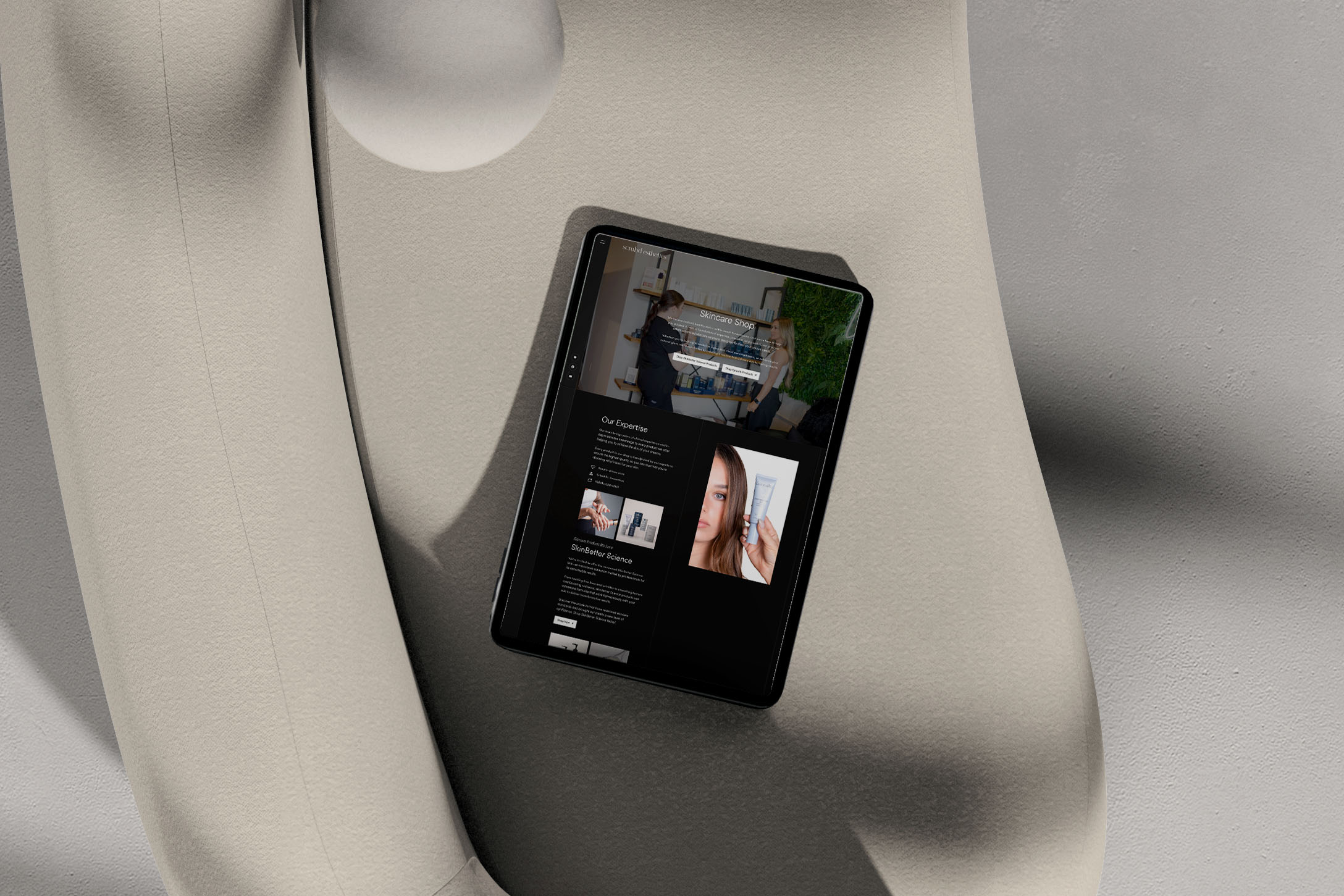 Scrubd Esthetics Skincare Shop page design shown on a tablet resting on a sculptural cream surface