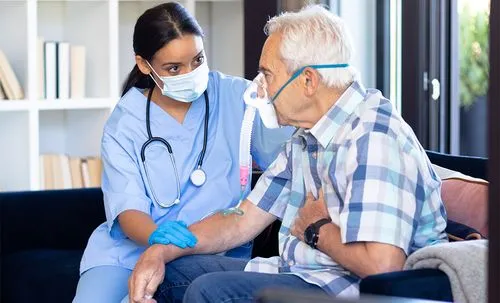 Female nurse in mask examines elderly male patient during home medical consultation visit.