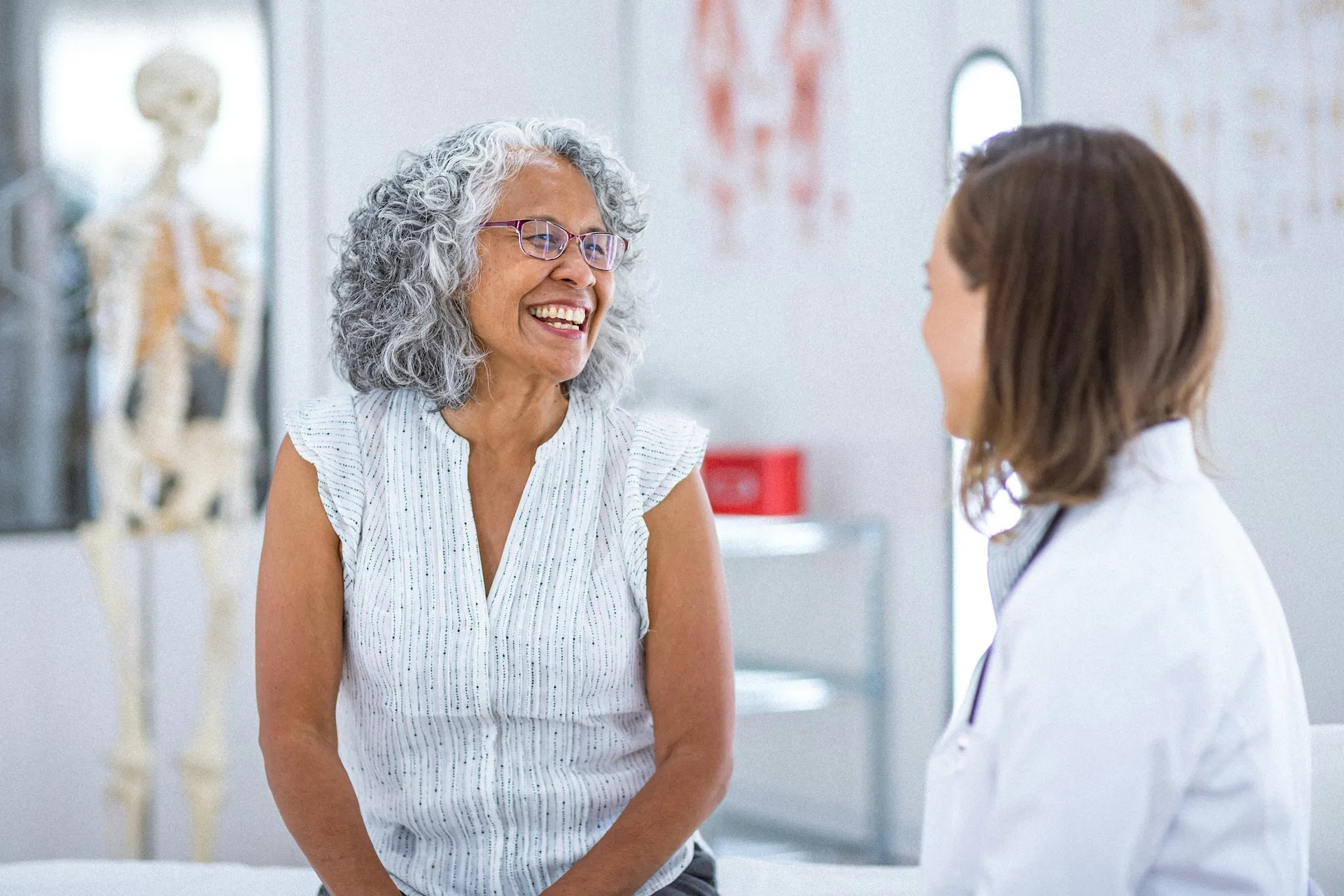 Smiling older woman with gray hair talking to female healthcare provider in medical office