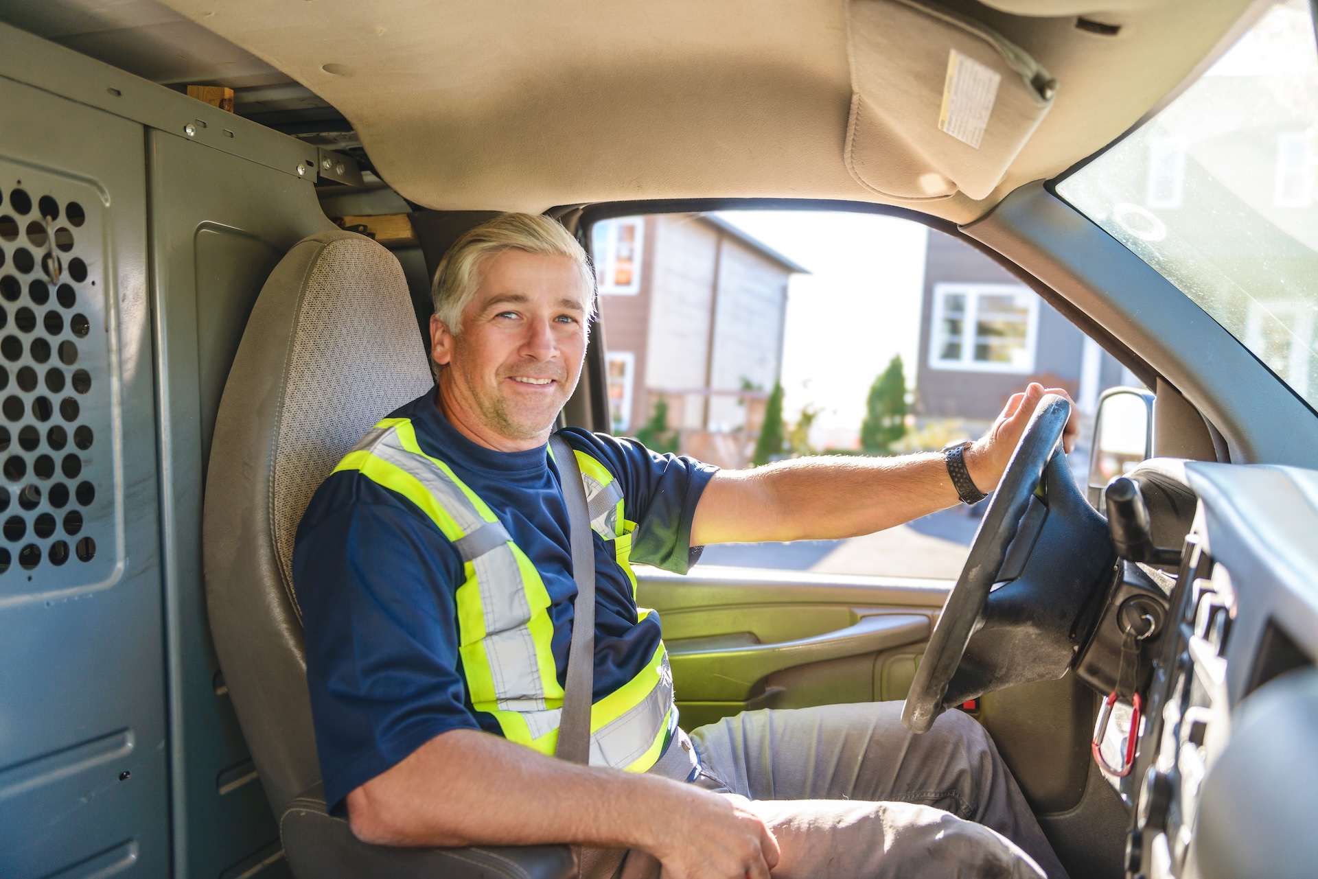 Male driver wearing safety vest smiling while sitting in vehicle cab