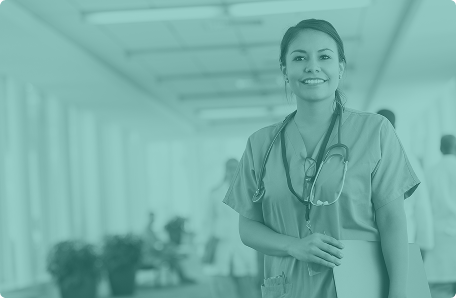 Smiling female medical worker in scrubs with a stethoscope around her neck standing in a hospital corridor.