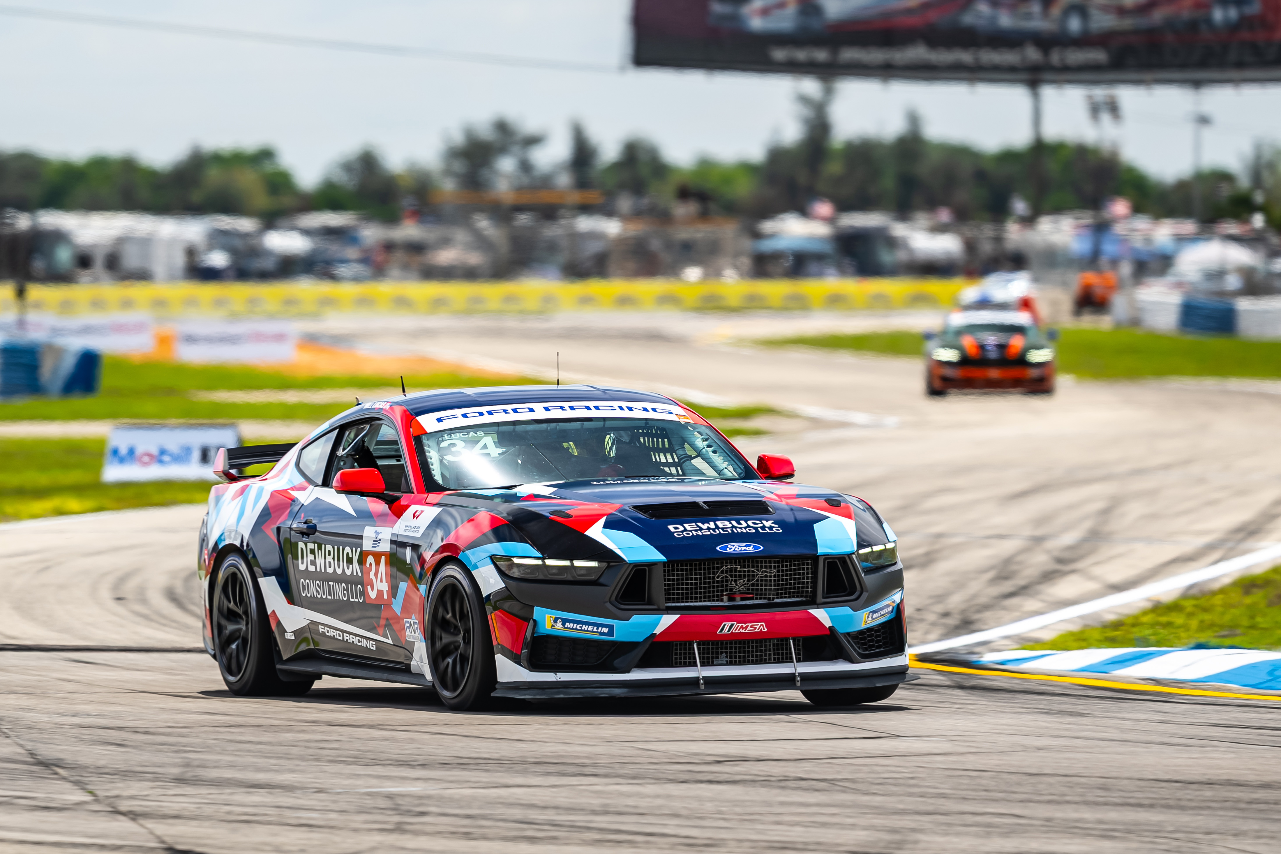 Ford Mustang race car number 34 with Dewbuck Consulting LLC branding on a race track.