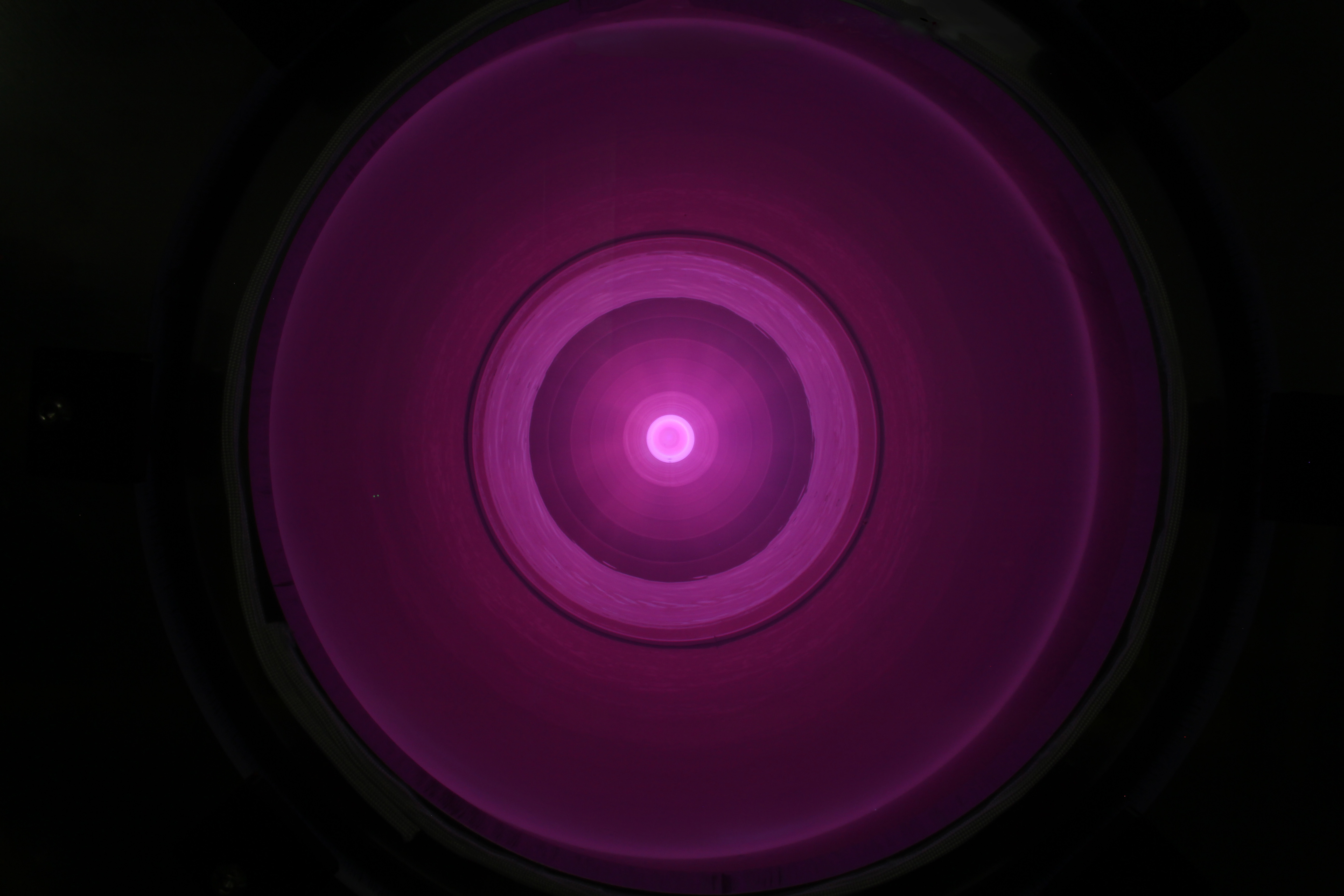 Circular pattern of concentric glowing pink rings with a bright center against a dark background.