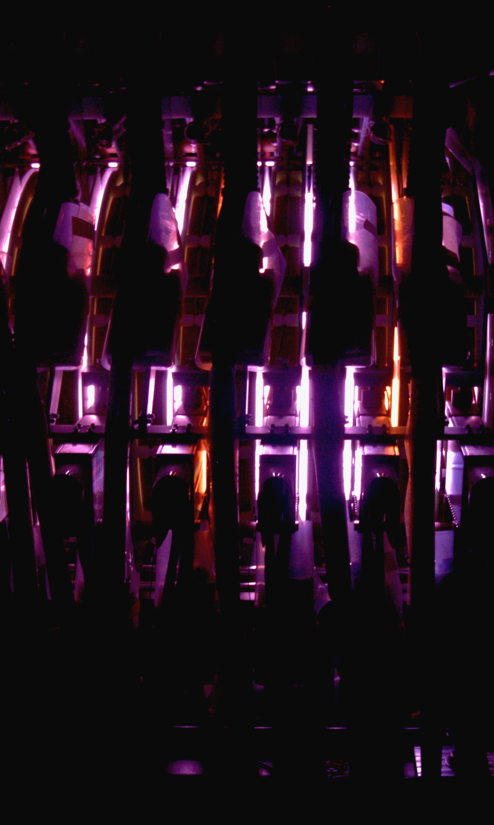 Dark industrial setup with multiple vertical views of glowing pink plasma.
