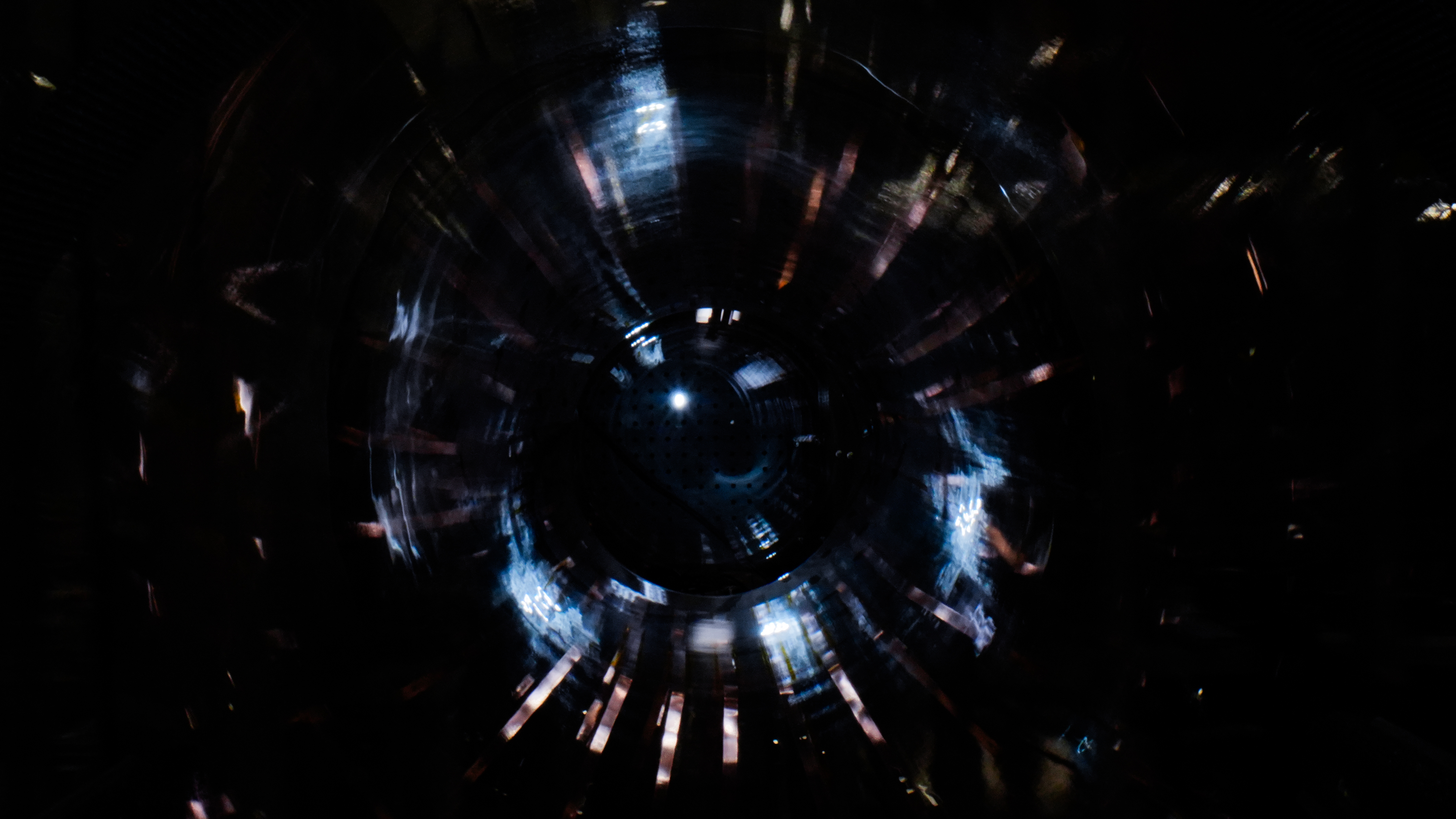 Abstract circular pattern with dark center and radiating blue and white light streaks.