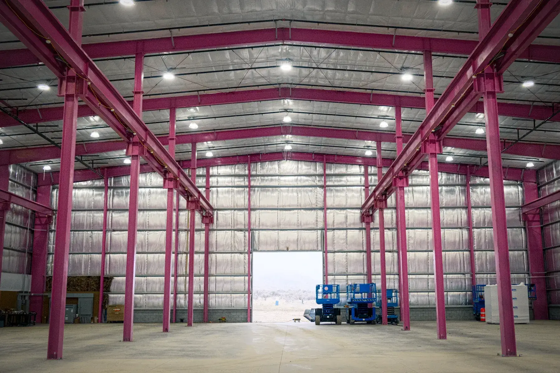 Spacious empty industrial warehouse with pink steel beams and bright ceiling lights.
