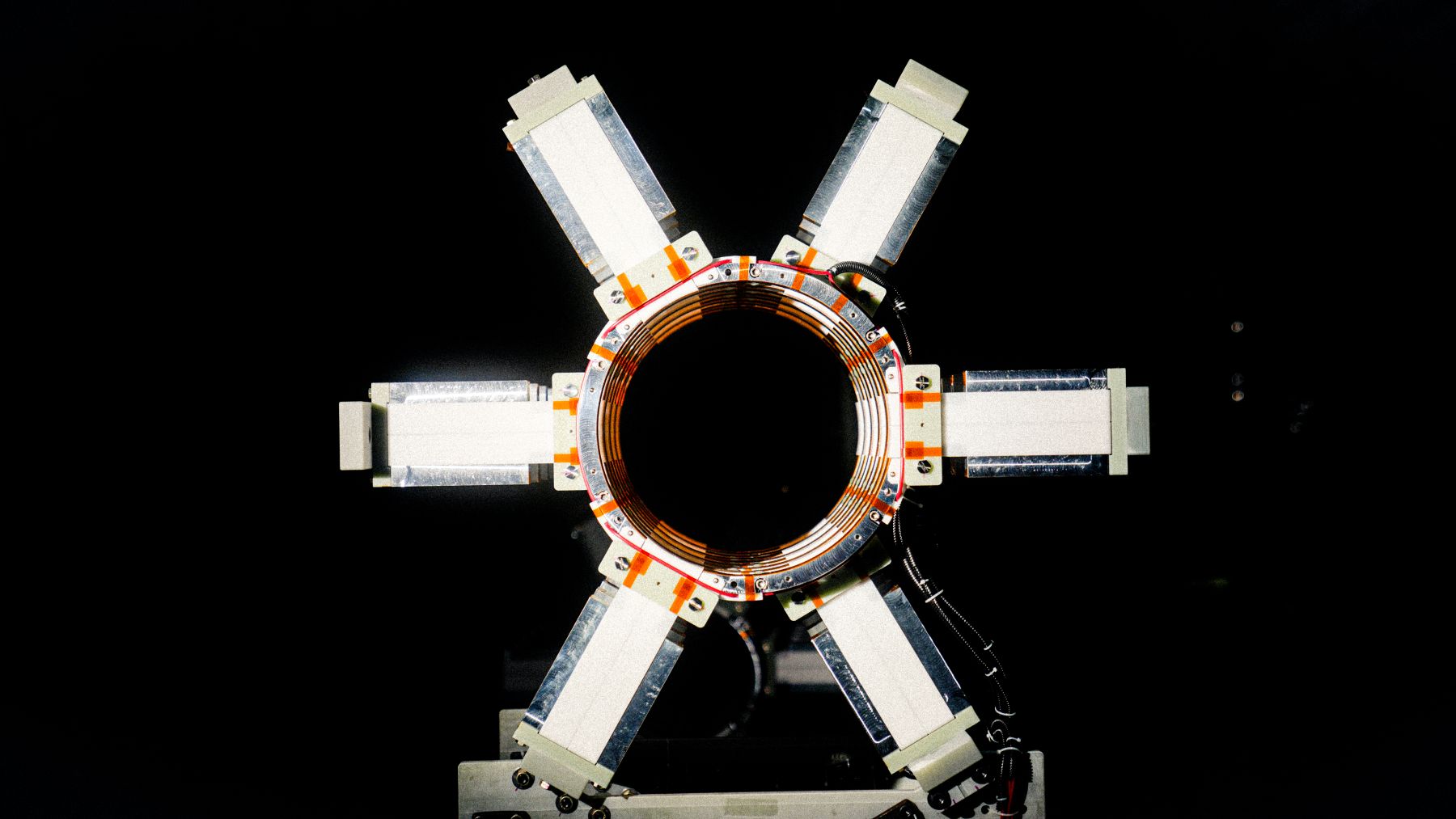 A circular mechanical component with six metal arms extending outward, against a black background.