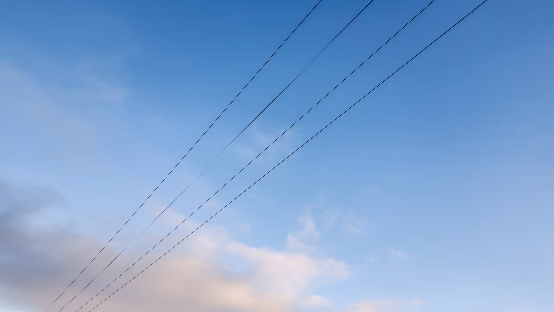 Blue sky with sparse white clouds and four parallel power lines running diagonally.