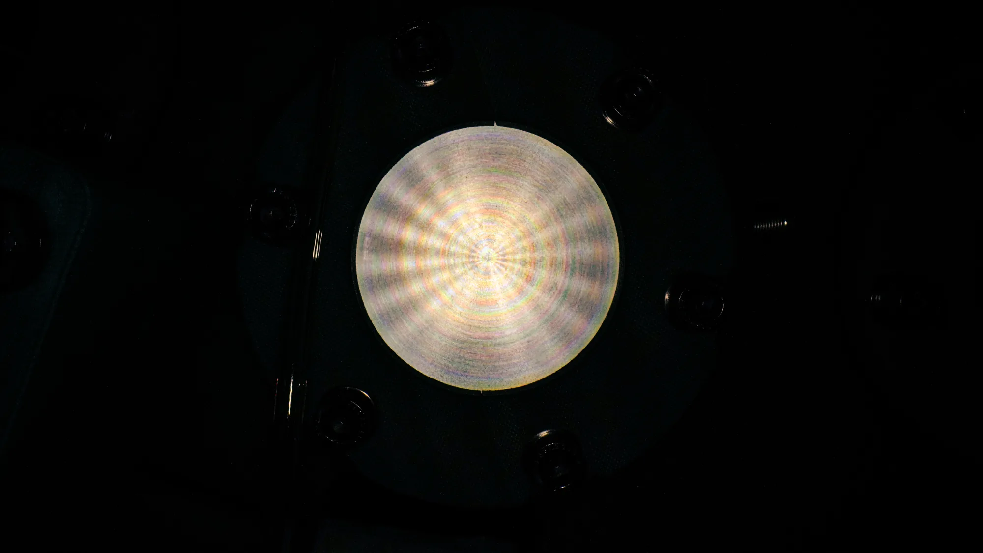 Close-up of a circular metallic surface with concentric texture and reflective patterns under low light.