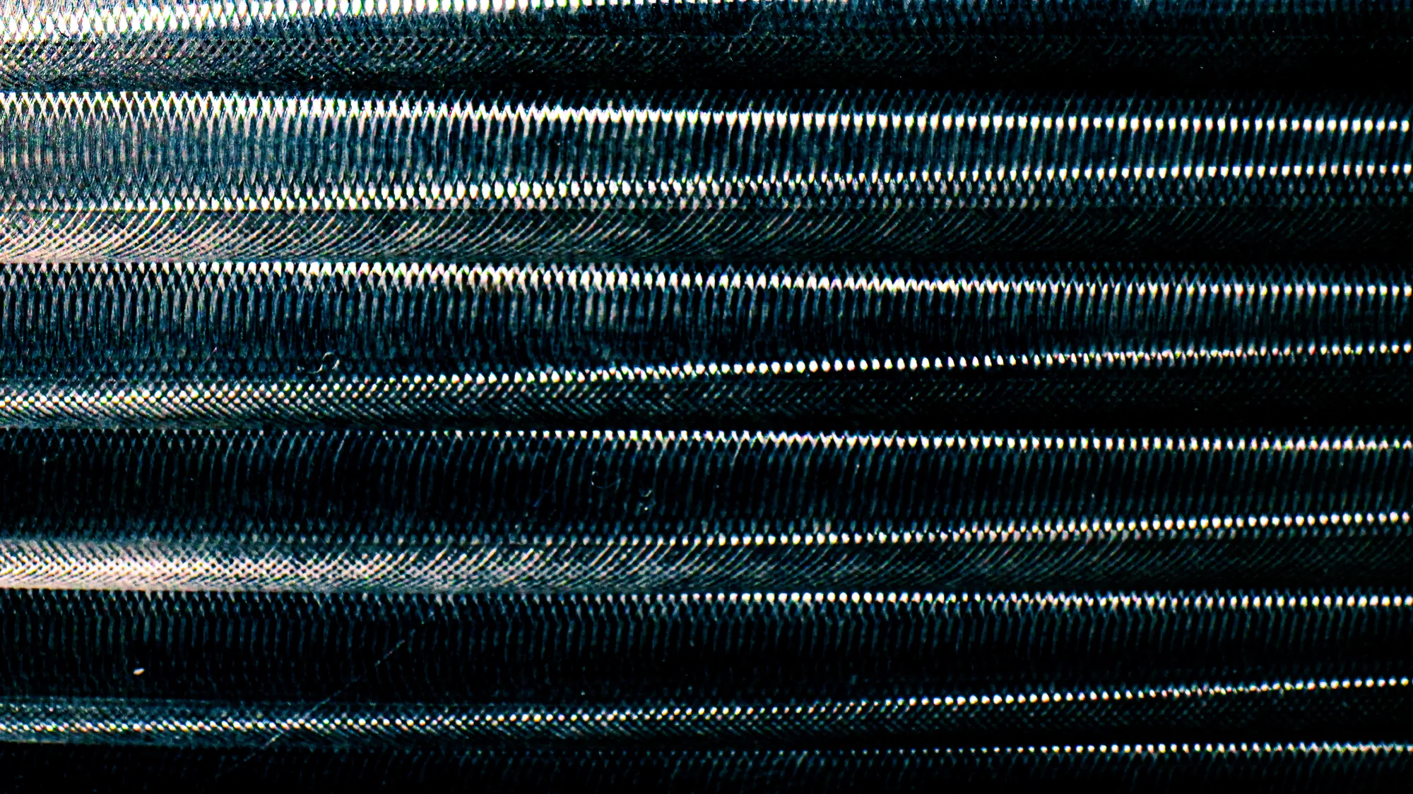 Close-up of a textured, ribbed metallic pattern and small white highlights.