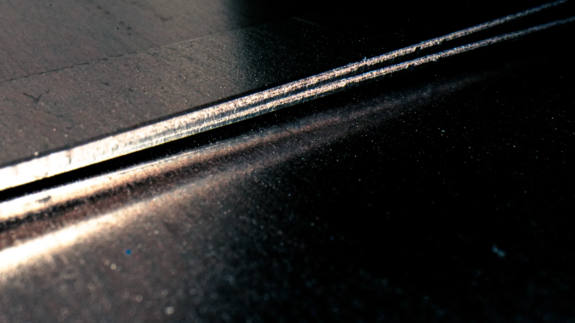 Close-up of a metallic surface edge with textured light reflection on a dark background.