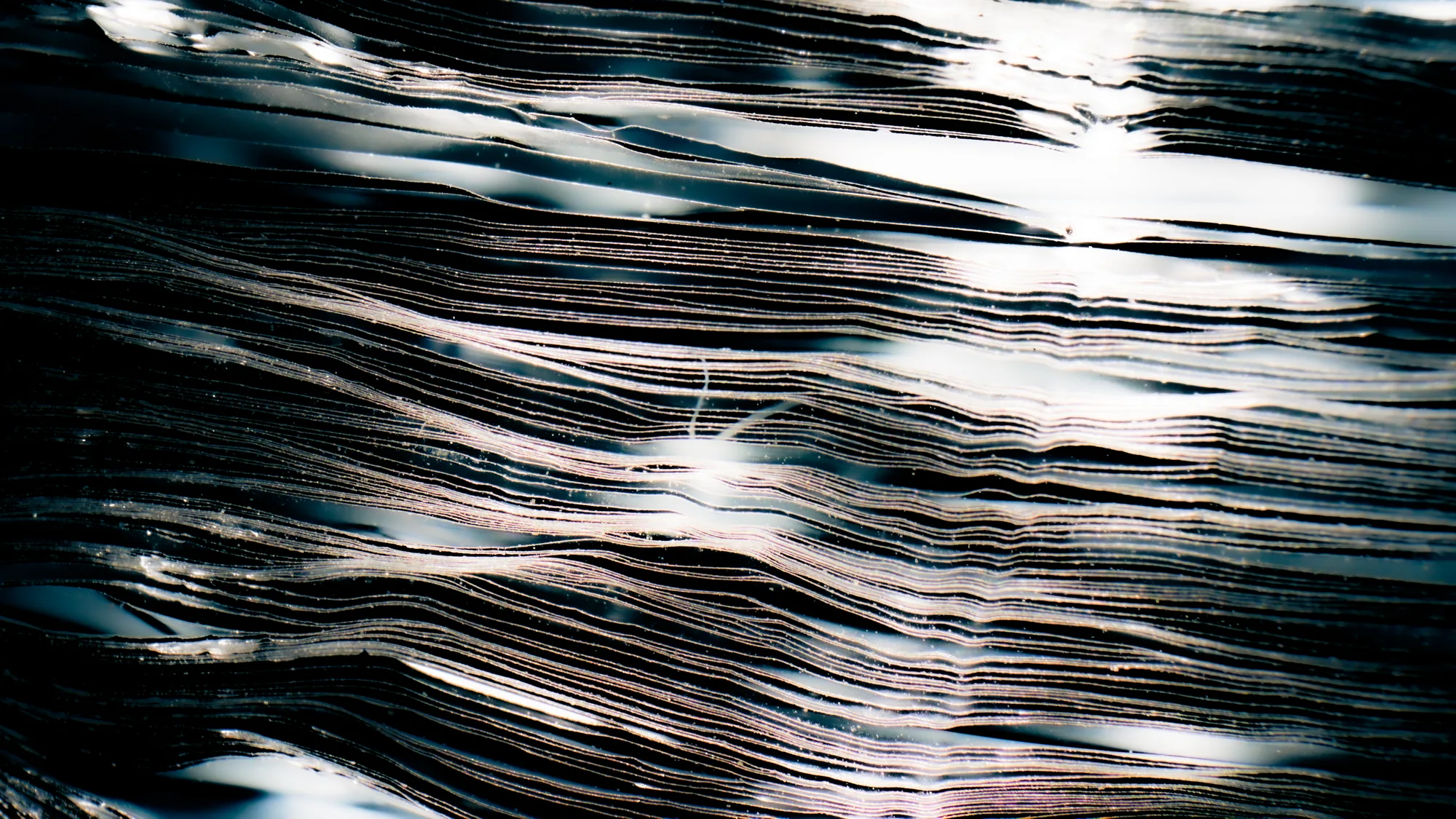 Close-up of silver metallic layered texture with light reflections creating abstract patterns.
