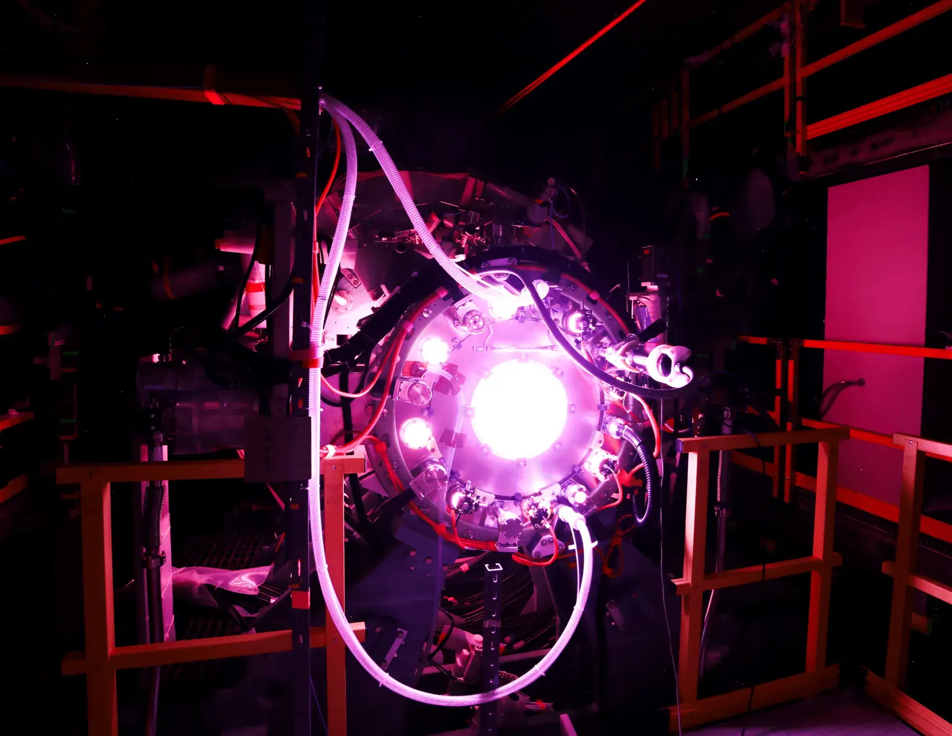 Brightly glowing machine with cables and tubes inside a dark industrial setting.