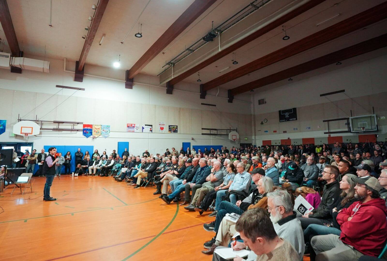 Helion CEO David Kirtley speaking at a community meeting in a school gym hall.