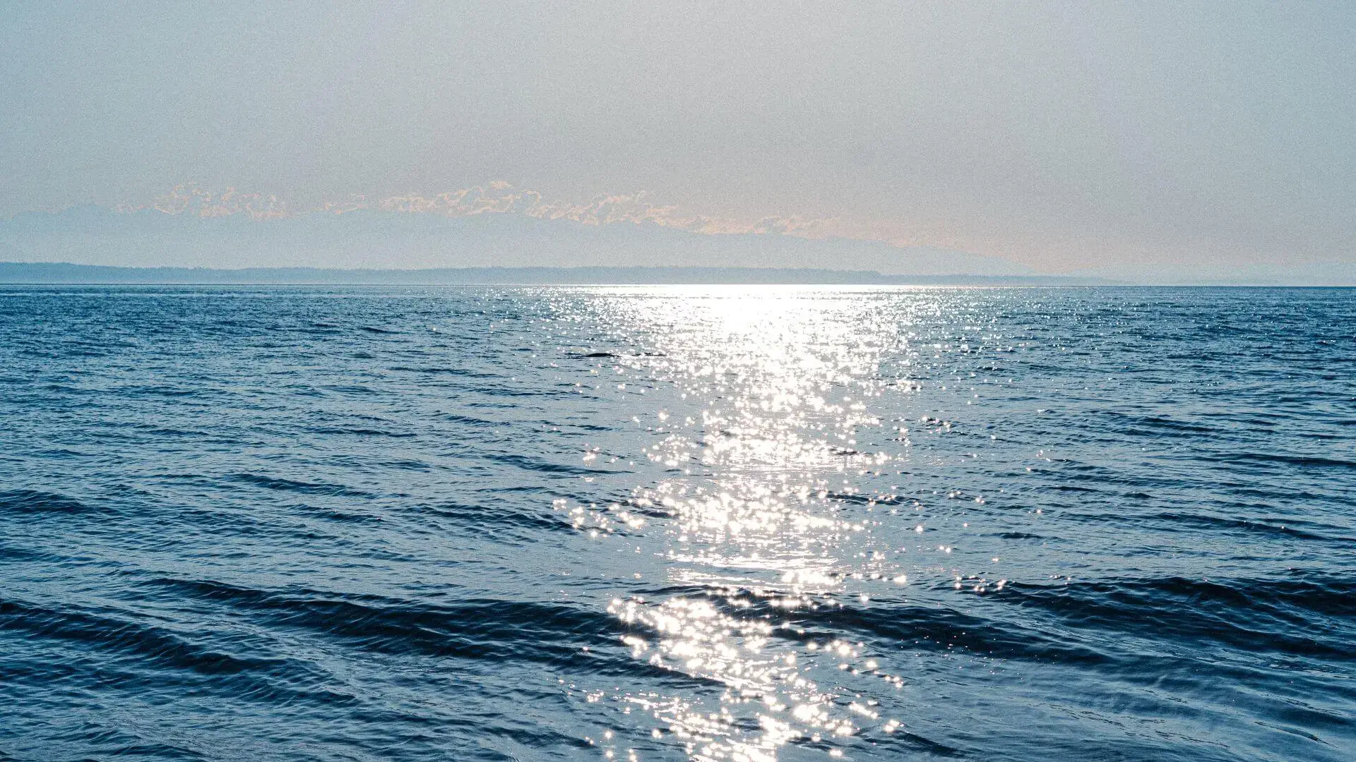 Sunlight reflecting on the calm blue ocean water with a distant horizon and faint clouds.