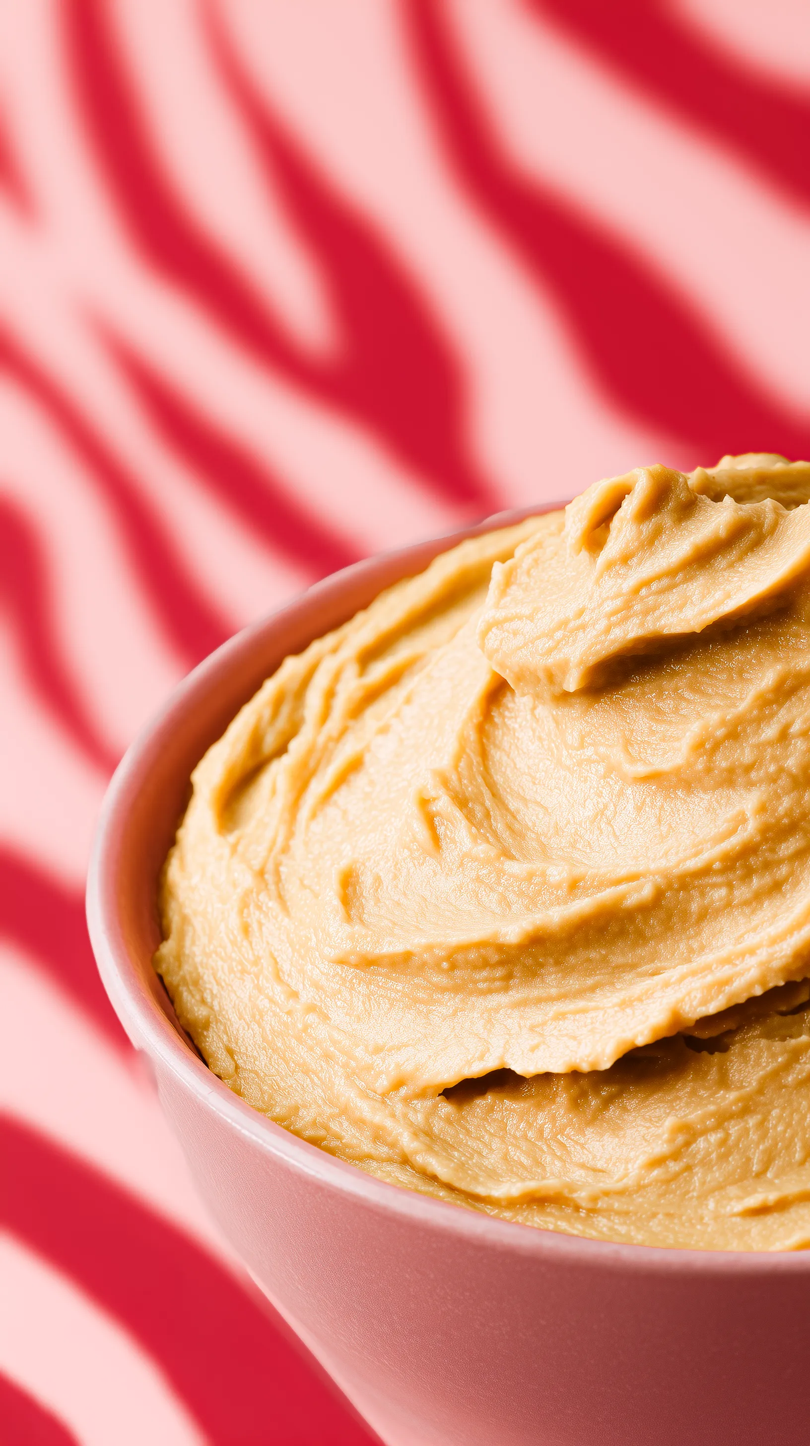 Close-up of a pink bowl filled with creamy peanut butter on a red and white striped background.