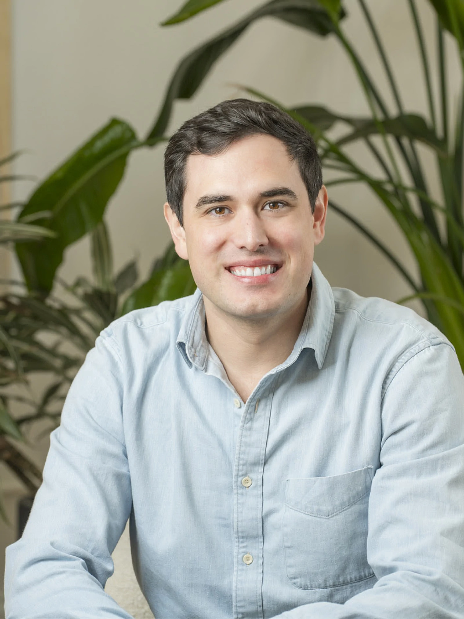 Team member headshot in front of a lush green plant
