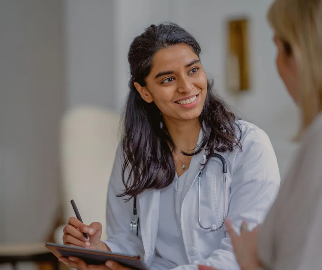 Smiling female doctor with stethoscope discussing with a patient while holding a tablet and pen.