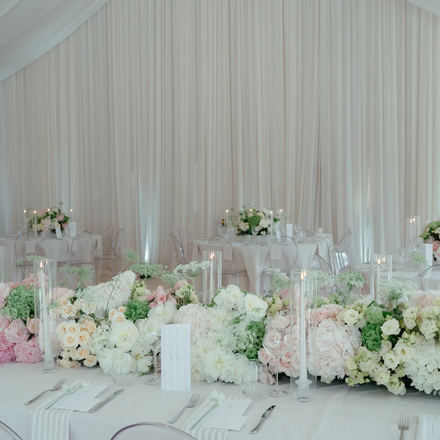 Elegant wedding reception table with white, pink, and green floral centerpiece and tall candles in glass holders.