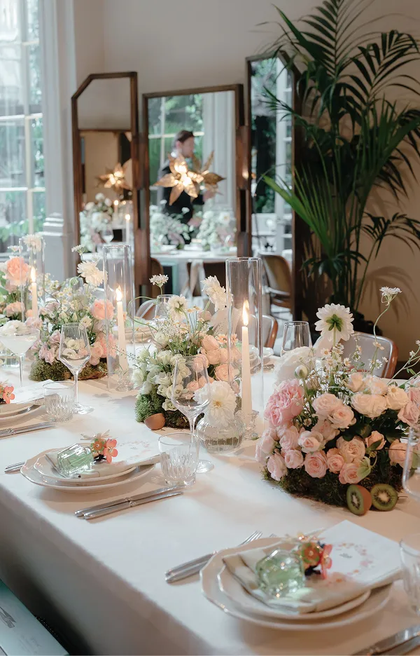 Elegant table setting with white linens, pink and white floral arrangements, and lit taper candles.