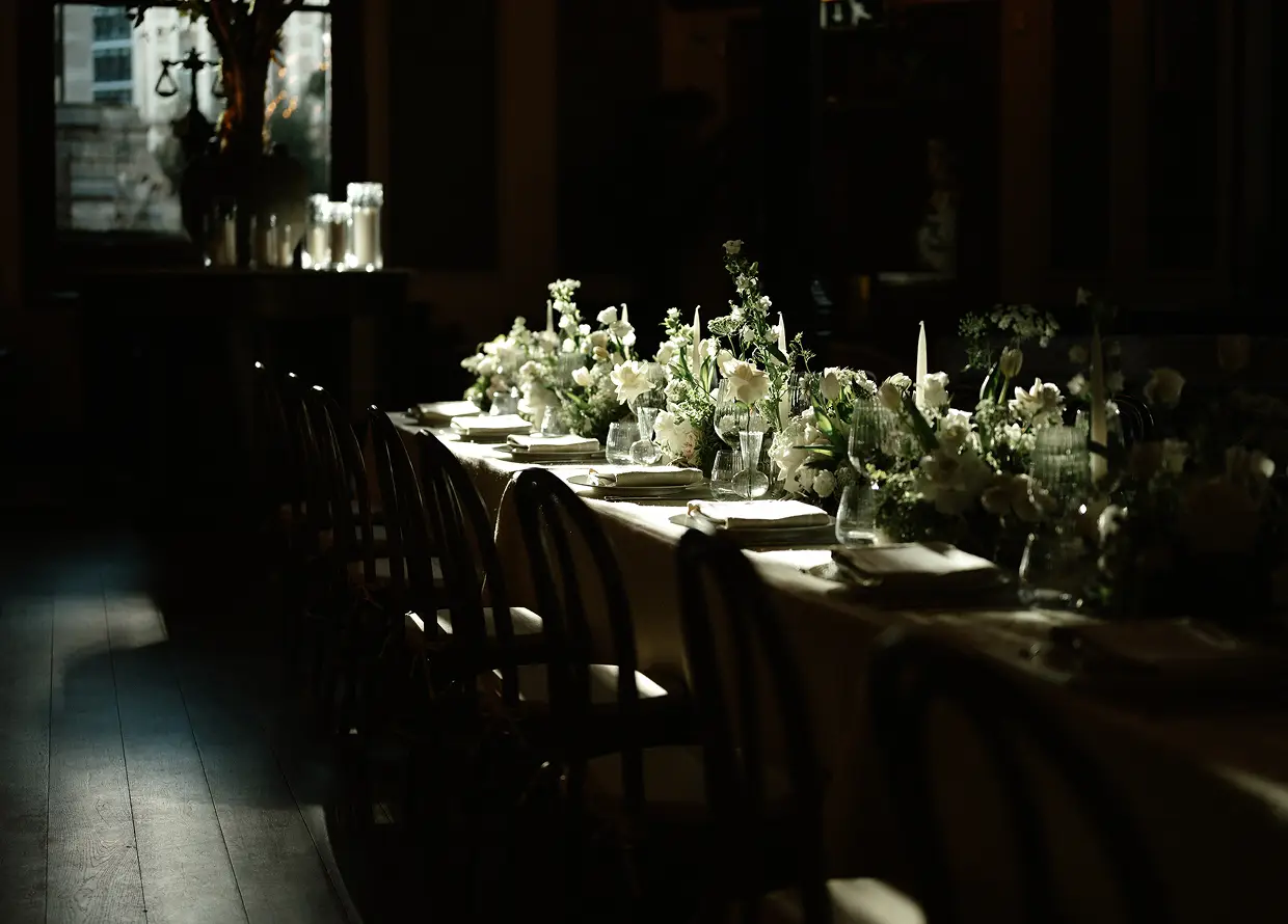Long dining table with white flowers, candles, and glassware in soft evening light.