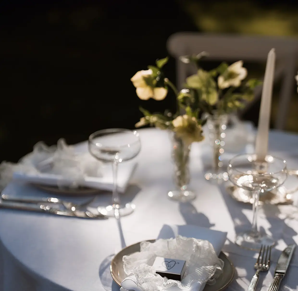 Elegant wedding table setting with white lace napkin, champagne glasses, flowers, and candlelight.