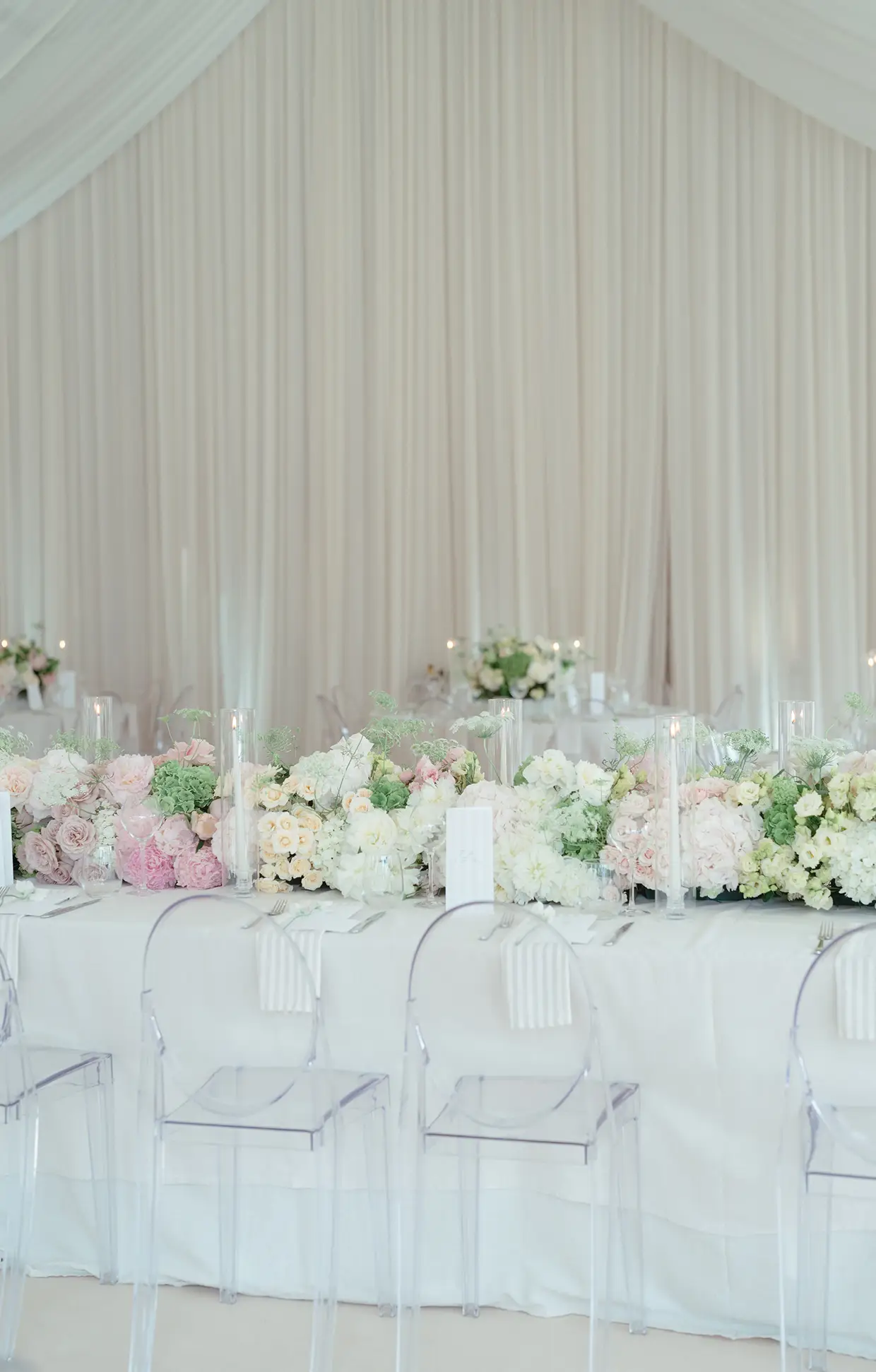 Elegant wedding reception table with white and pastel floral centerpiece and clear ghost chairs.