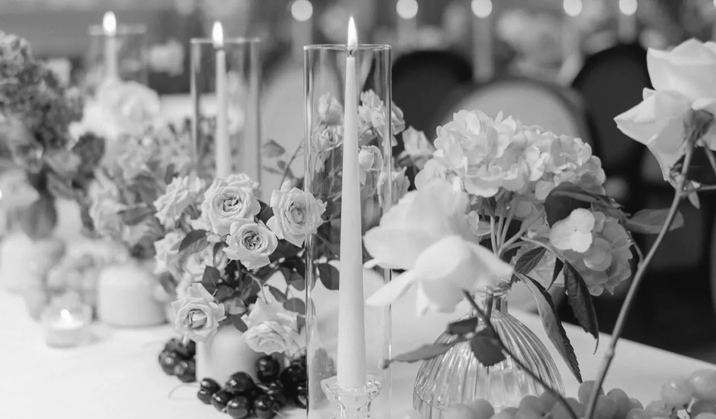 Table decorated with lit taper candles in glass holders and floral arrangements including roses and hydrangeas.