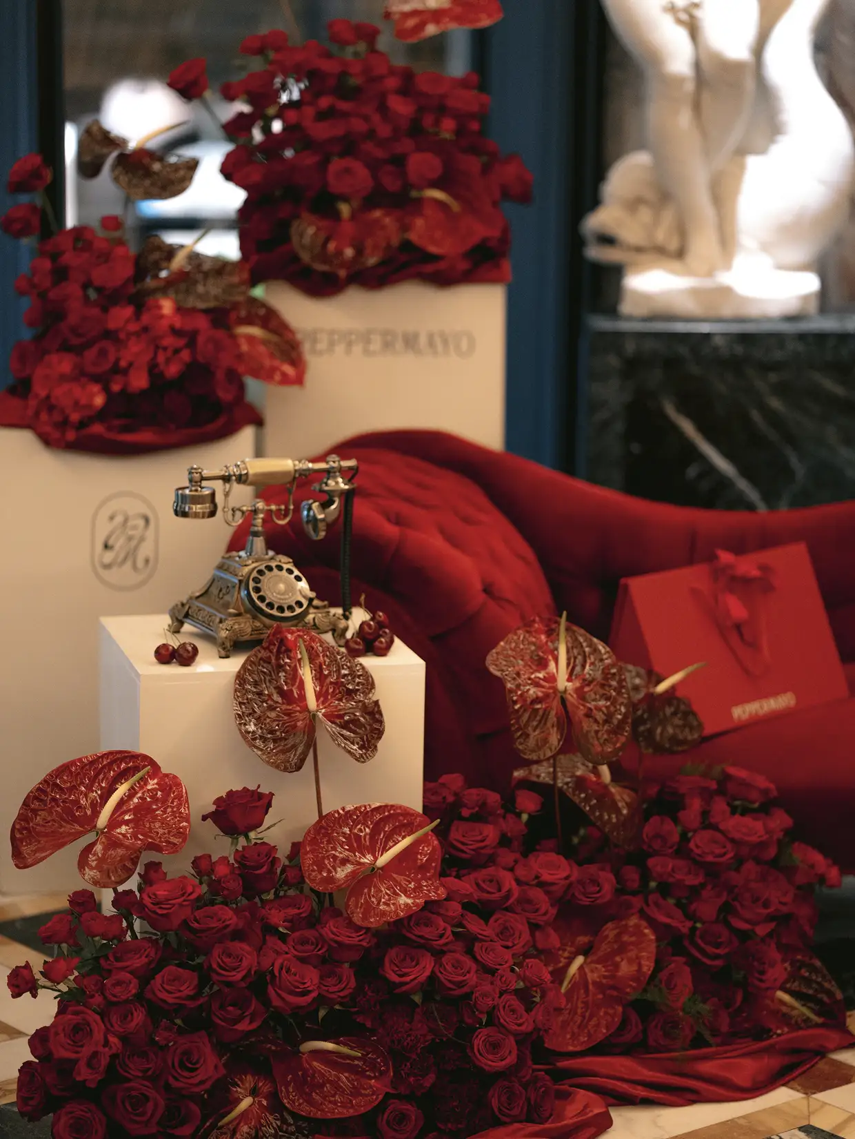 Vintage rotary telephone surrounded by red roses and anthurium flowers in an elegant indoor setting.