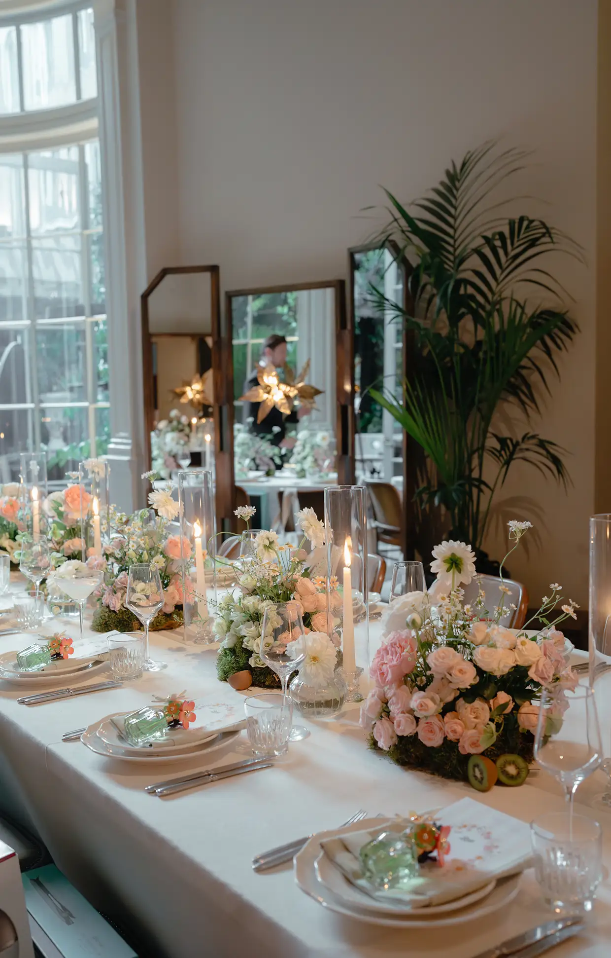 Elegant dining table with white tablecloth, floral centerpieces, lit candles, and neatly arranged glassware and plates.