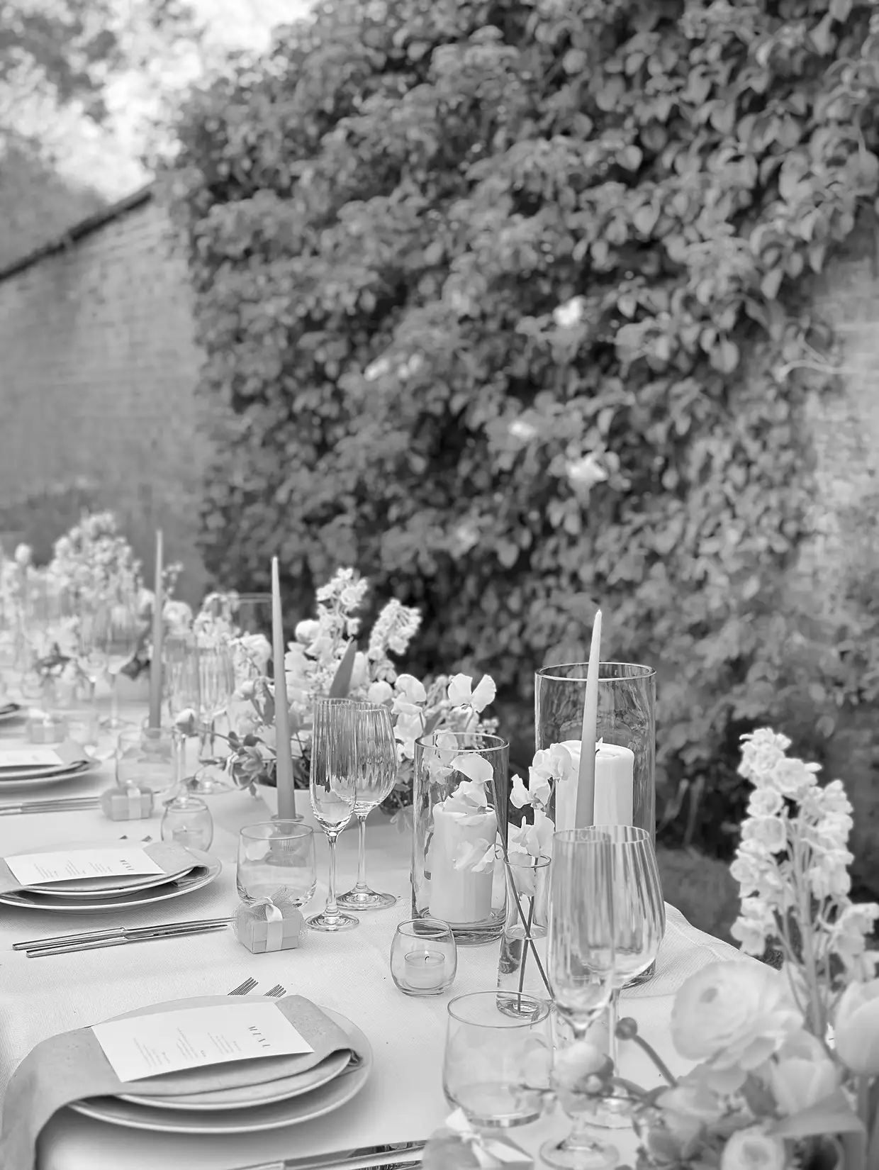 Elegant outdoor dining table with plates, glasses, candles, and floral centerpieces set for an event.