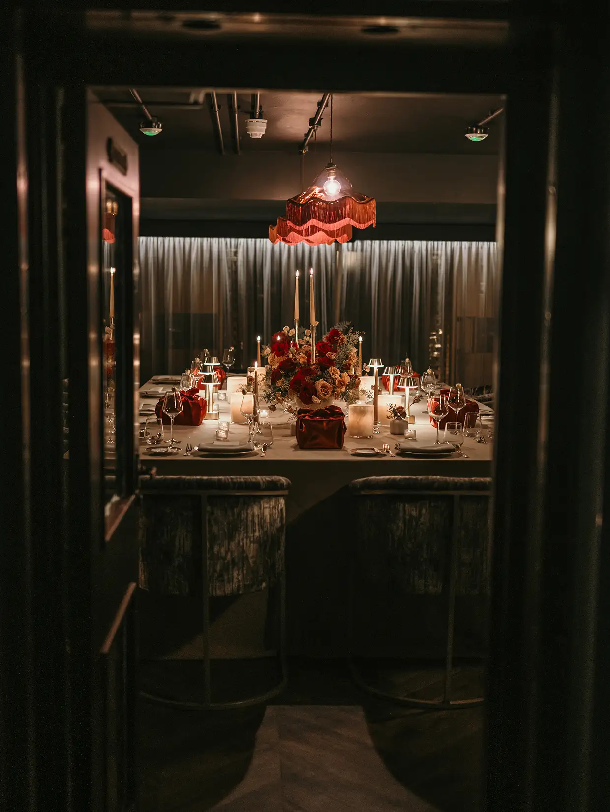 Elegant dining table set with floral centerpiece, candles, wine glasses, and red decor under warm pendant light.