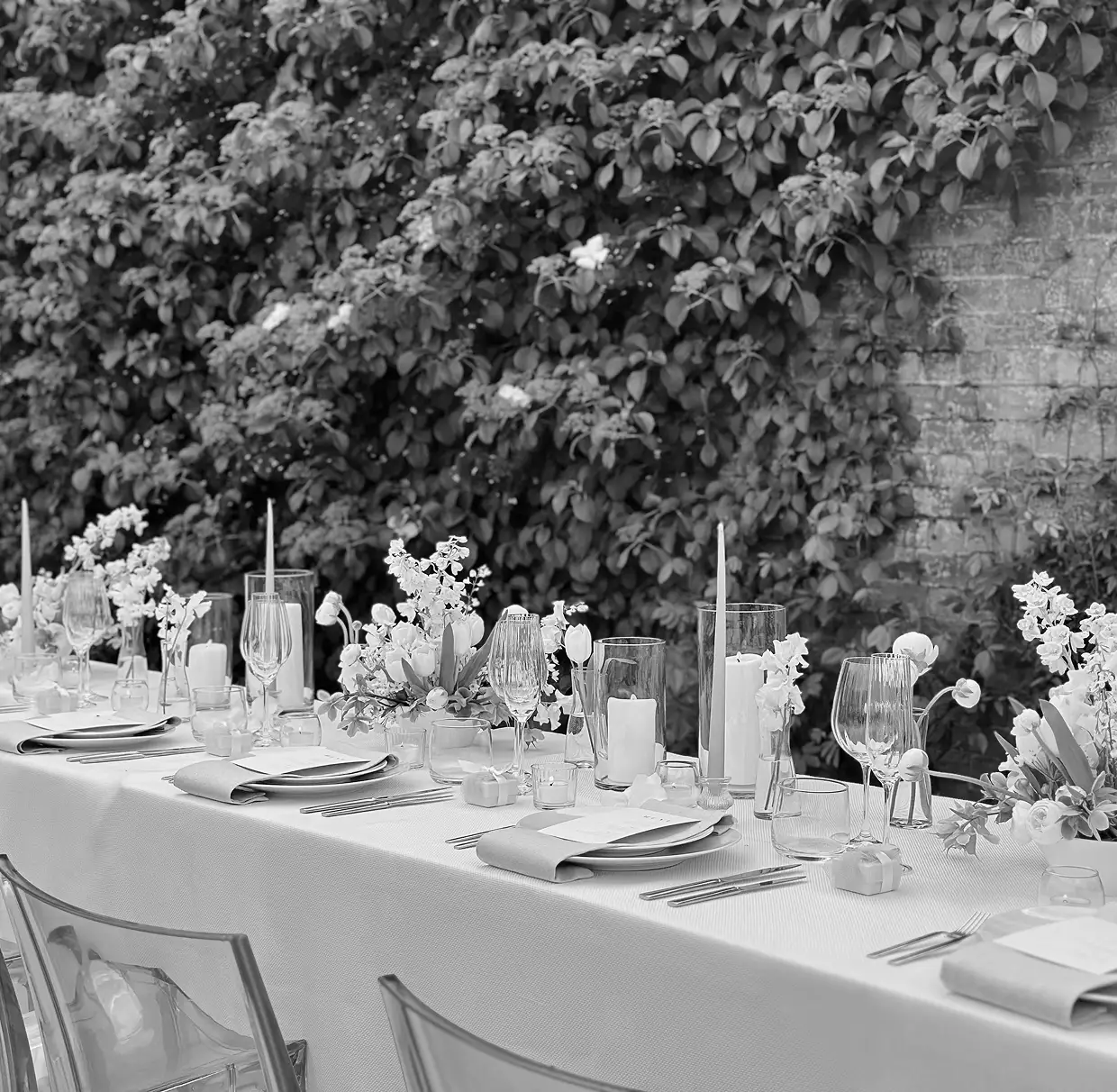 Elegant outdoor dining table set with white tablecloth, floral centerpieces, candles, and glassware.