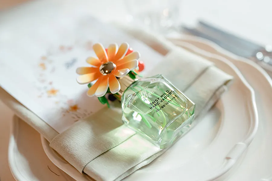 Small bottle of Marc Jacobs Daisy Wild perfume with a flower-shaped cap on a folded napkin over a white plate.