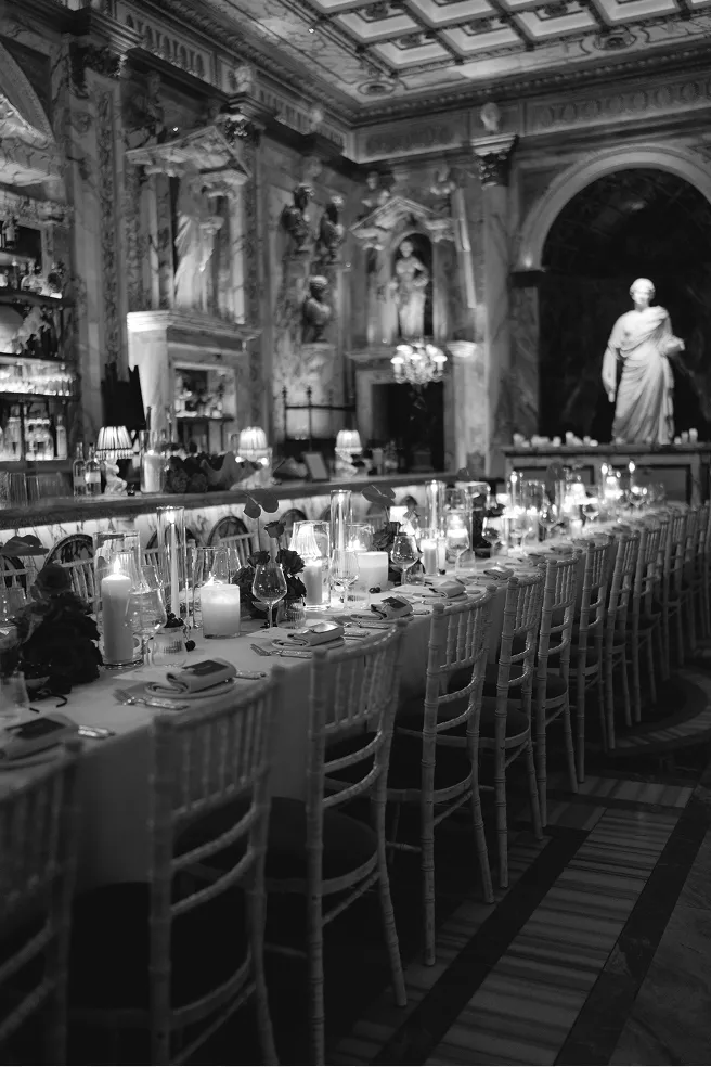 Long elegant dining table set with candles and glassware in ornate room with classical sculptures.