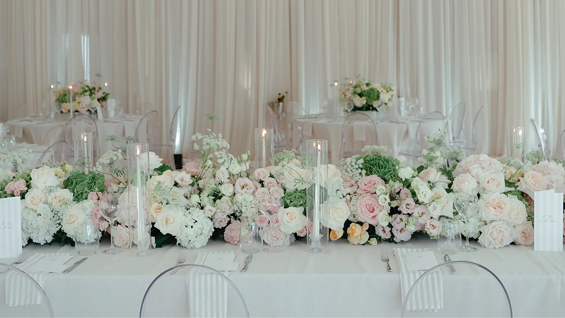 Elegant wedding table with white and pink floral centerpiece and tall glass candle holders.