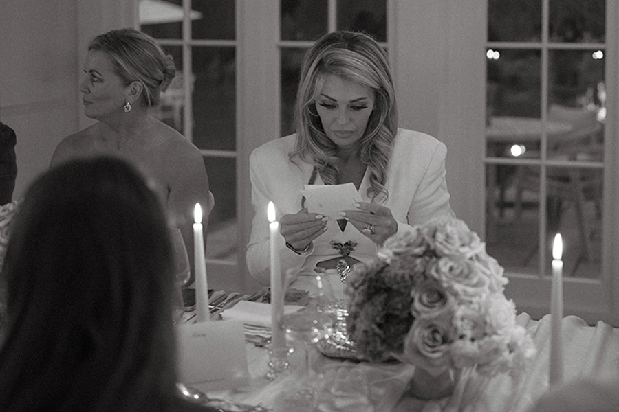 Woman in white blazer reading a card at a candlelit dinner table with floral centerpiece.