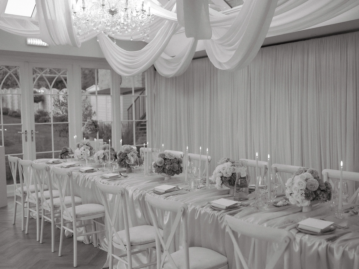 Elegant long dining table with floral centerpieces, candles, and white chairs in a decorated indoor room.
