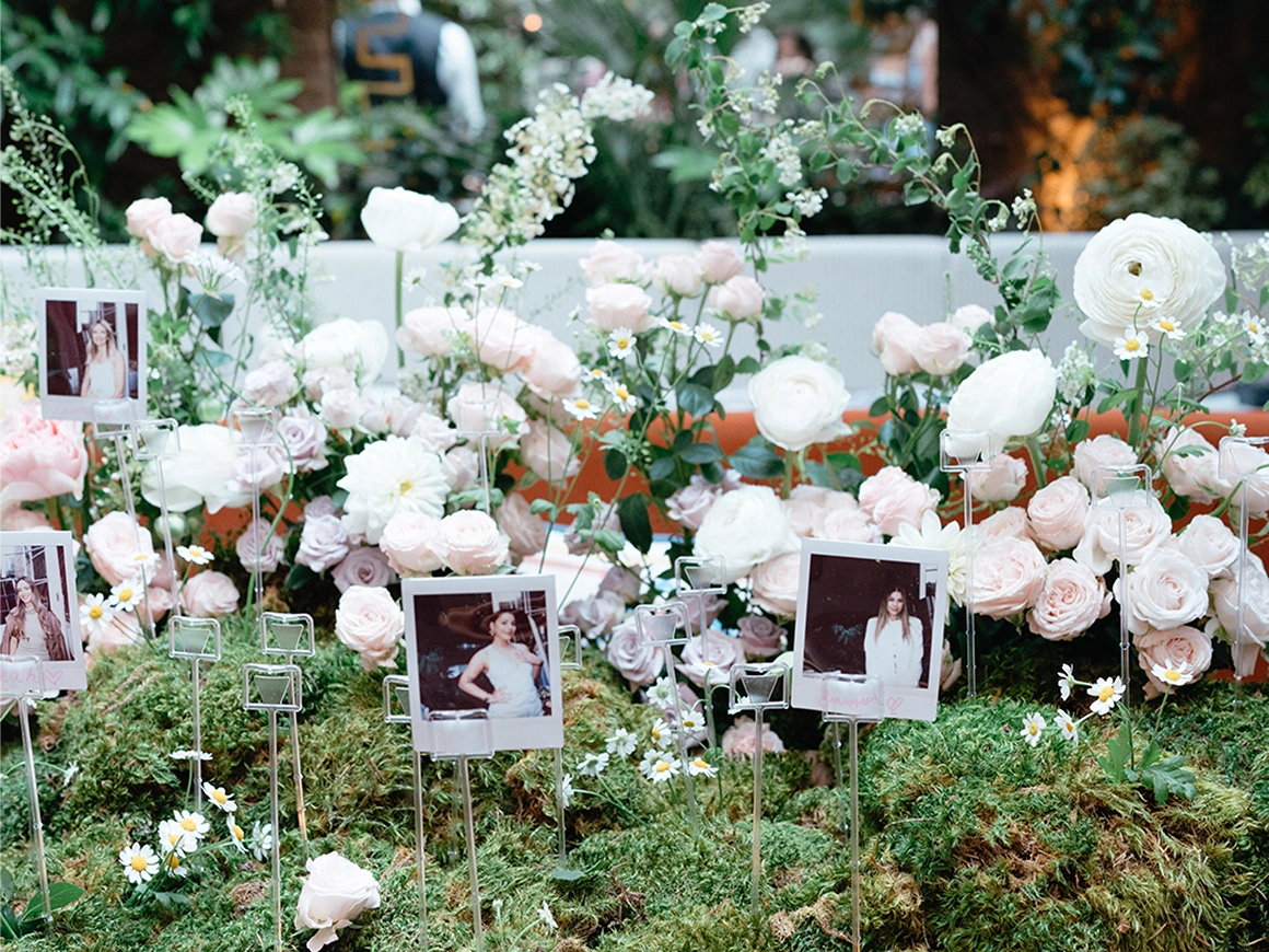 Decorative arrangement of pale pink and white flowers with moss and photos on metal holders.