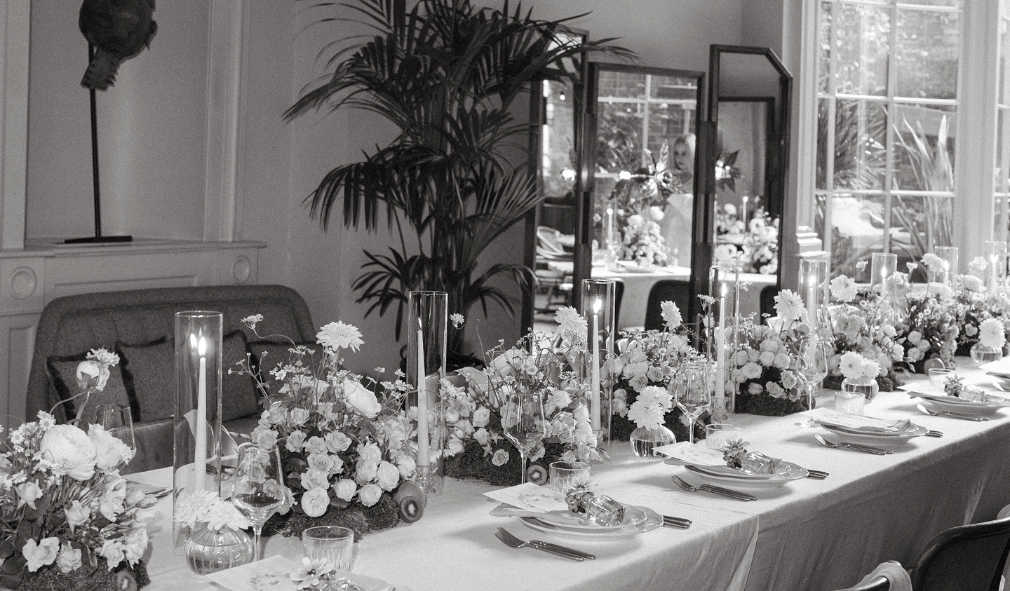 Long dining table set with floral centerpieces, tall candles, glassware, and plates in an elegant room.