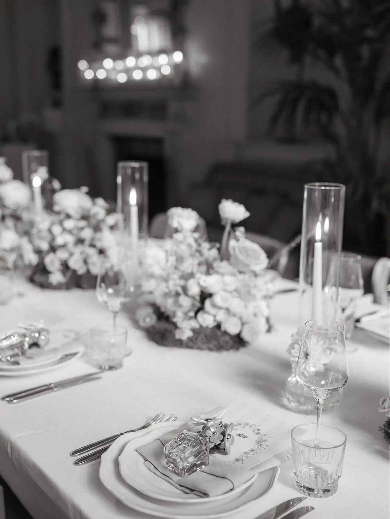 Elegant dining table with floral centerpiece, lit candles, wine glasses, and neatly arranged plates and cutlery.