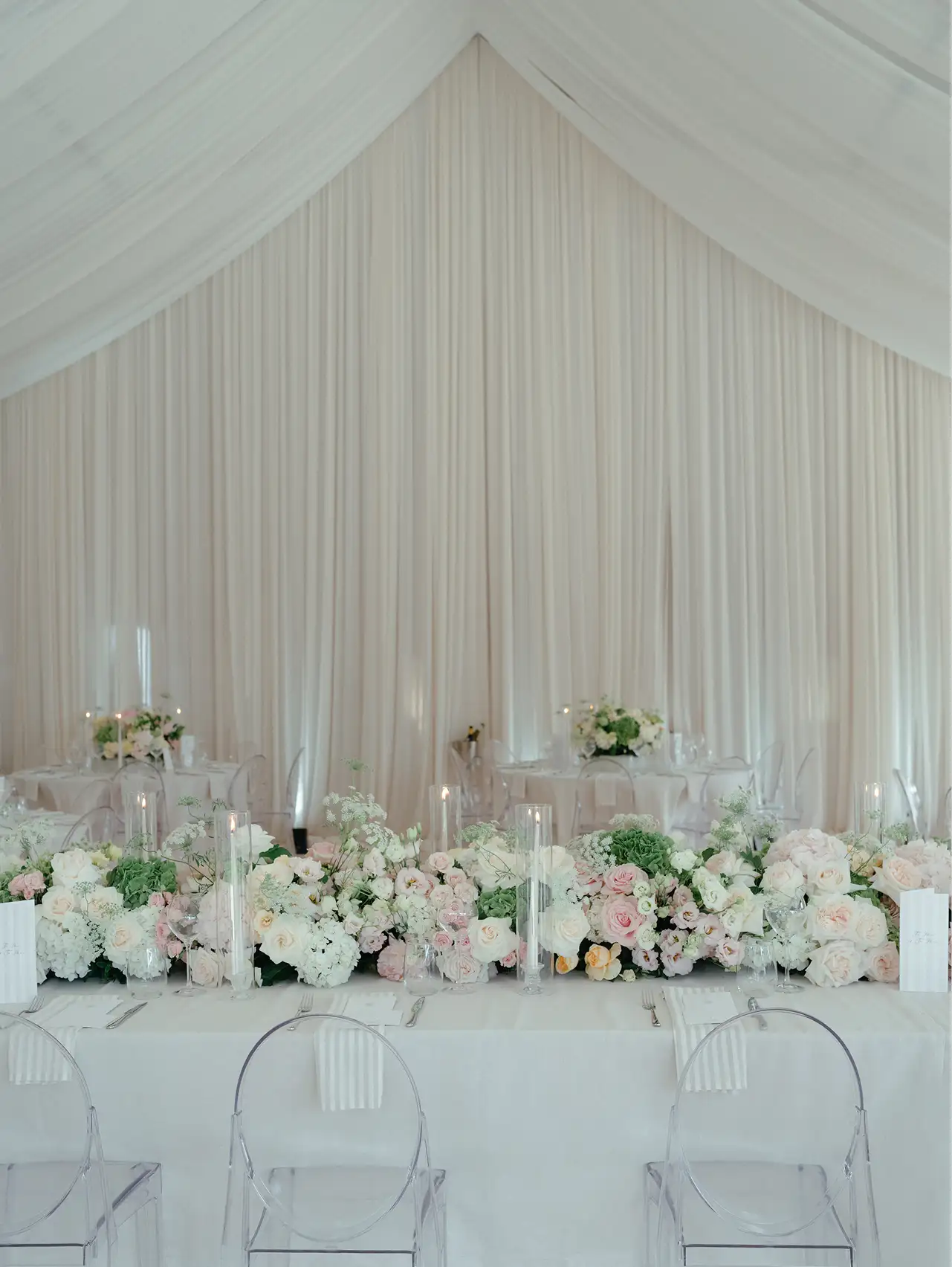 Elegant wedding reception table with white and pastel floral arrangements and clear ghost chairs.