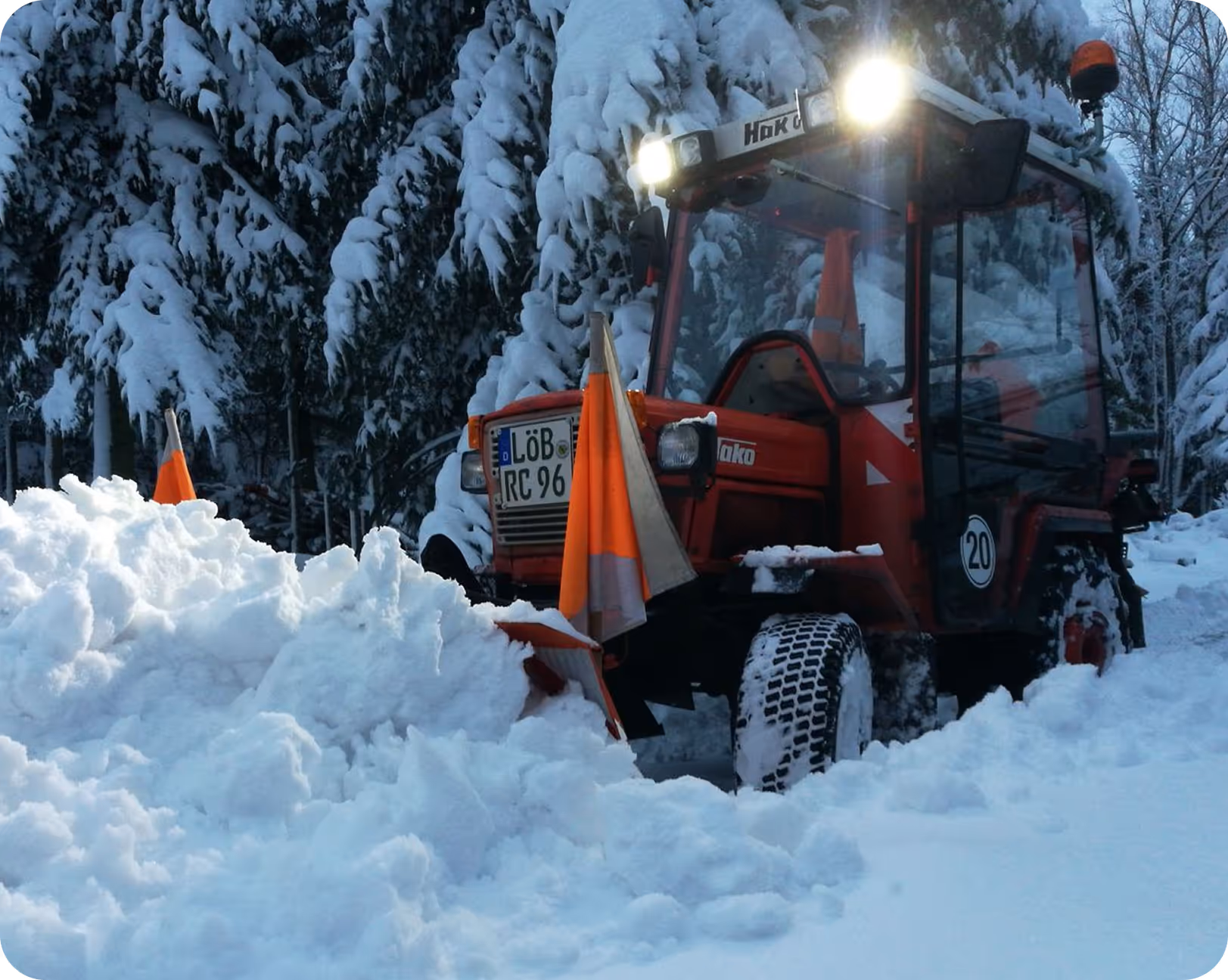 Roter Schneepflug beseitigt Schnee auf einer verschneiten Straße im Wald.
